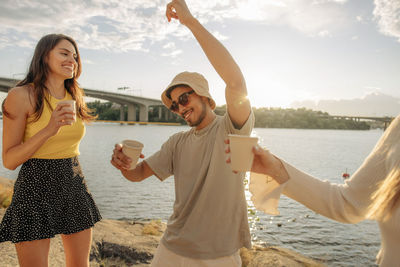 Carefree young man dancing with hand raised by female friends during picnic