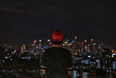 Rear view of man looking at illuminated city buildings