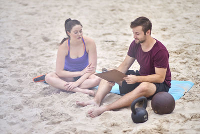 Young woman sitting with fitness instructor at beach