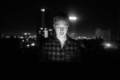 Portrait of young man looking at illuminated city at night