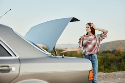 Rear view of woman with umbrella standing against car