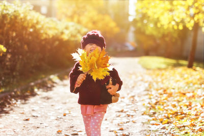 Cheerful girl holding autumn leaf while walking at park