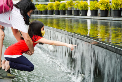 Cute girl wearing mask touching flowing water outdoors