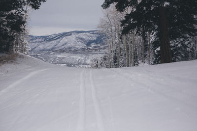 Road by snow covered landscape against sky