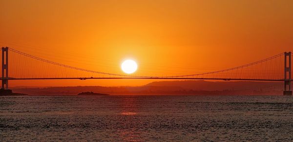 Scenic view of suspension bridge over sea against orange sky