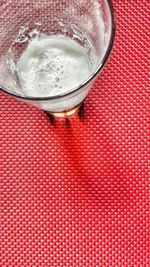 Directly above view of frothy beer in glass on red tablecloth