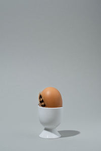 Brown egg in white eggcup with brown feather. gray background, space for text. easter card.