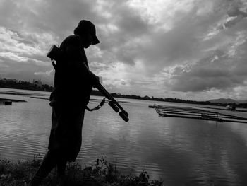 People fishing in sea against cloudy sky