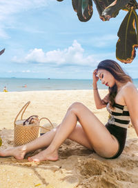 Young woman sitting on shore at beach against sky