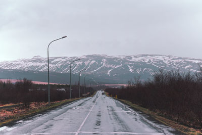 Diminishing perspective of road leading towards snowcapped mountains against sky