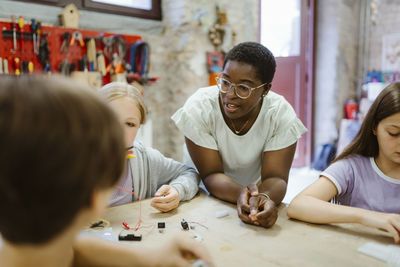 Female teacher leaning on table while teaching students during technology class