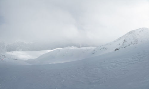 Mountain landscape of a snowy valley without people, sunlight breaks through a foggy cloud