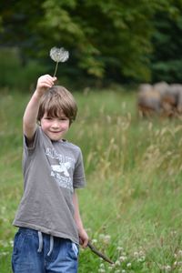 Boy standing on field with dandelion clock