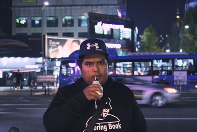 Portrait of young man standing against illuminated city at night