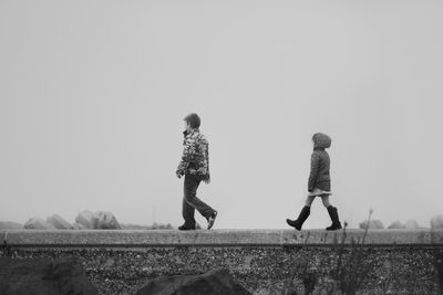 Siblings walking on field against clear sky