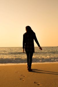 Rear view of woman walking on beach against clear sky