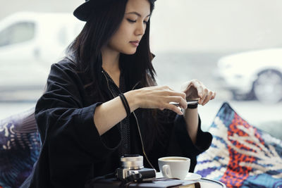 Young woman photographing coffee through smart phone in creative office