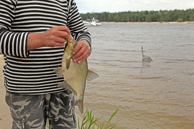 Midsection of man holding fish while standing by river