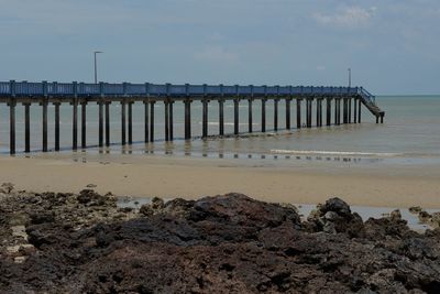 Wooden posts on beach by sea against sky