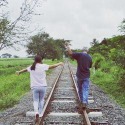 Rear view of man and girl walking on railway tracks