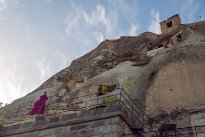 Woman in a long purple dress stands at the entrance to the rock in cappadocia