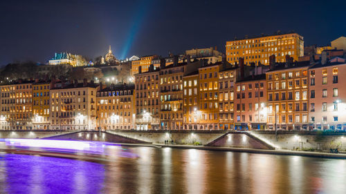 Illuminated city by river against sky at night