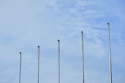 Low angle view of poles against cloudy sky