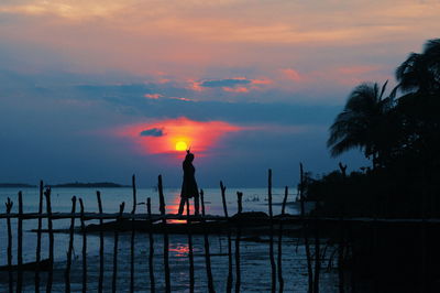 Silhouette man by sea against sky during sunset