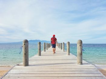 Rear view of man standing on pier at sea against sky
