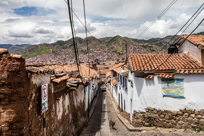 Diminishing perspective of road amidst houses against cloudy sky during sunny day