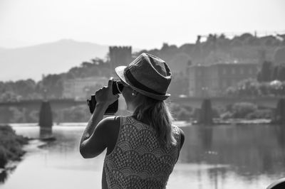 Woman holding hat standing against sky in city