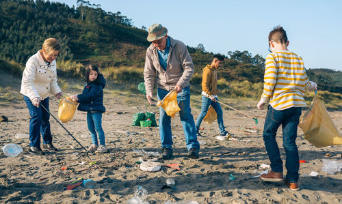 Grandparents and grandchildren cleaning while standing at beach