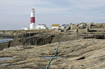 Lighthouse amidst buildings and sea against sky