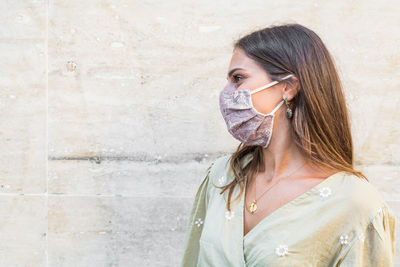 Smiling young woman wearing mask standing against wall outdoors