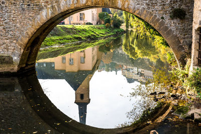 Arch bridge over river amidst trees and buildings