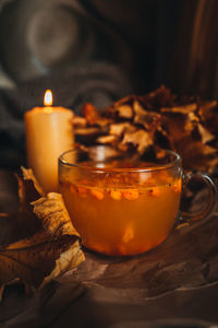 Burning candle and a mug of hot orange sea buckthorn tea in a cozy home autumn evening still life