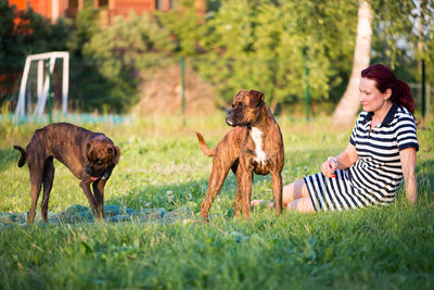 Mid adult woman playing with dogs while sitting on grassy field against sky at park