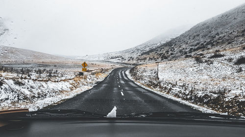 Road amidst snowcapped mountains against sky during winter