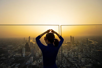 Rear view of man standing by buildings against sky during sunset