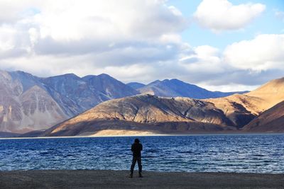 Rear view of man standing on mountain by sea against sky