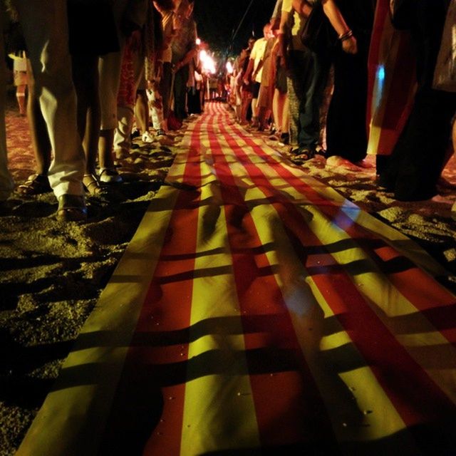 illuminated, night, the way forward, diminishing perspective, vanishing point, in a row, street, city, lighting equipment, incidental people, architecture, built structure, transportation, road, outdoors, person, building exterior, walking, city life, group of people