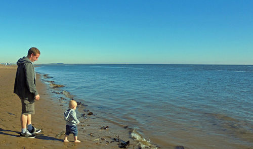 Father and son walking at beach against clear blue sky