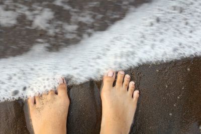 Low section of woman standing on wet sand