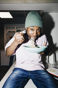 Portrait of young man eating noodles while sitting on dining table at college dorm