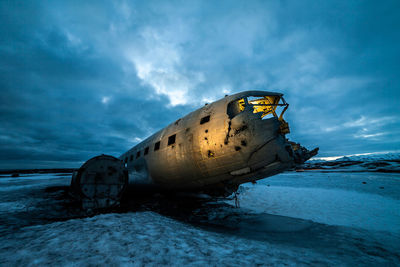 Abandoned airplane on snowy land by sea against sky