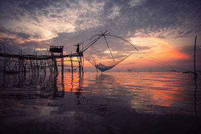 Silhouette fishing net by sea against sky during sunset