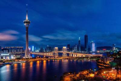 Illuminated buildings by river against sky at night