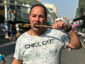 Portrait of mid adult man eating while standing on street in city