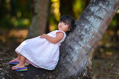Side view of girl lying on tree trunk in forest