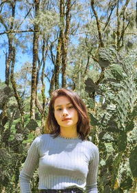 Portrait of young woman standing against trees